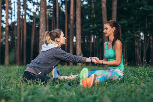 Dos amigas guapas practicando yoga juntas haciendo piernas anchas sentadas hacia adelante dobladas al aire libre —  Fotos de Stock