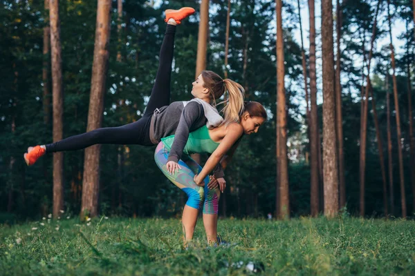 Dos jóvenes deportistas haciendo ejercicio de pareja juntas en el bosque — Foto de Stock