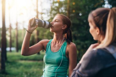 İki kadın koşucular egzersiz ayakta sonra rahatlatıcı parkta konuşan ağaç yakınındaki