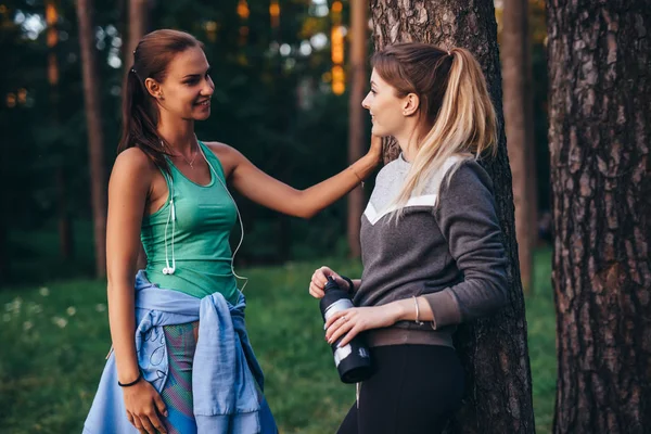 Two female runners relaxing after workout standing near the tree talking in park — Stock Photo, Image