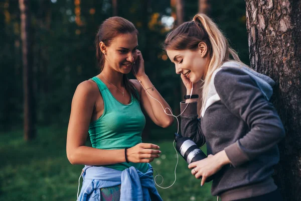 Twee vrouwelijke lopers ontspannen na training staan in de buurt van de boom praten in park — Stockfoto