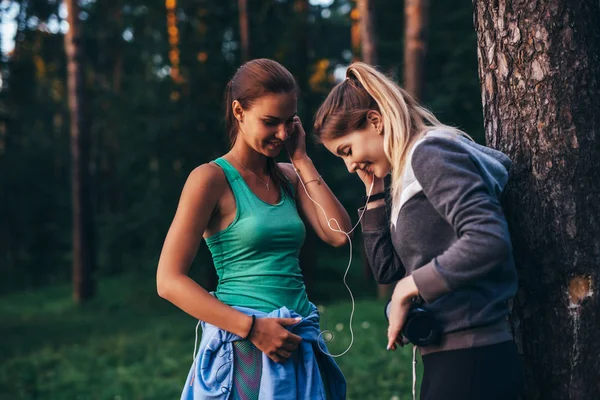 Two female runners relaxing after workout standing near the tree talking in park — Stock Photo, Image