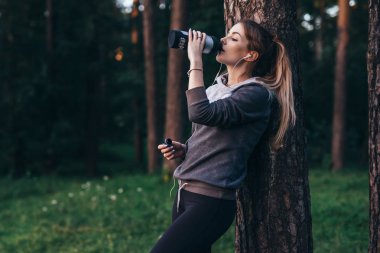 Kadın jogger yoğun egzersiz duran ağaç içme suyu yakınındaki sonra kurtarma parkta Kulaklık takmış