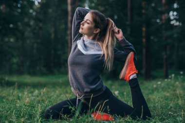 Genç kadının tek bacaklı güvercin yapıyor yoga uygulamak çim parkta oturup poz