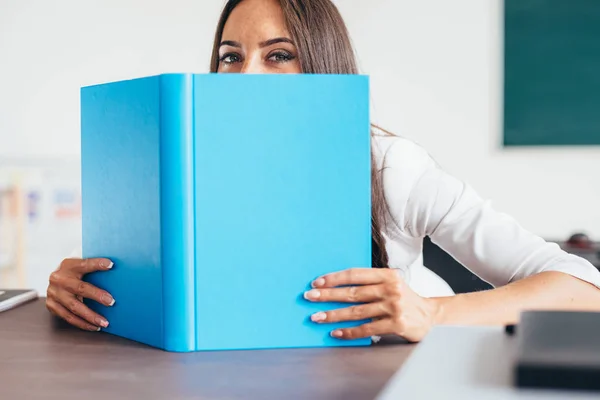 Estudante feminina escondendo o rosto atrás do livro olhando para a câmera . — Fotografia de Stock