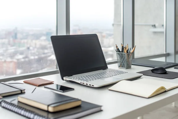 Werkplek met laptop laptop comfortabele werk tabel in office ramen en uitzicht op de stad. — Stockfoto