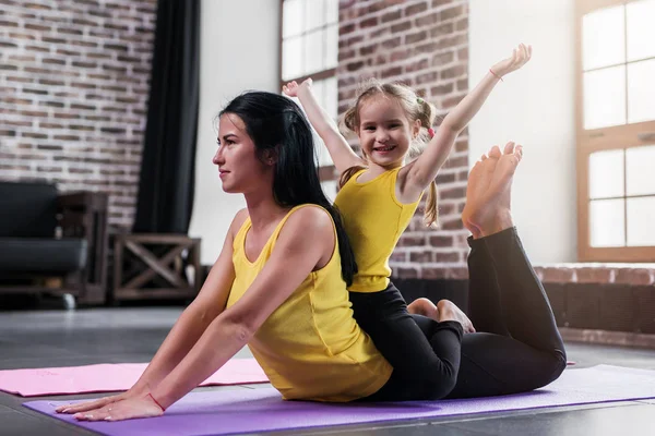 Joven madre caucásica haciendo yoga cobra pose en el suelo mientras su hija sonriente sentado en las mamás espalda —  Fotos de Stock