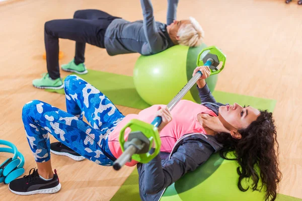 Sportlerinnen beim Langhantelpressen auf einem Schweizer Ball liegend beim Gruppentraining im Fitness-Center — Stockfoto