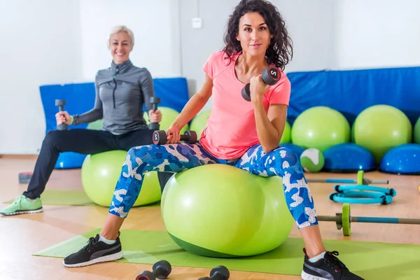 Gülümseyen ince beyaz kadın fitness topları ve kamera bir spor salonunda bakarak dumbbells ile yapıyor — Stok fotoğraf