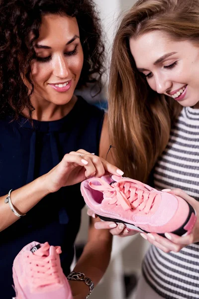 Two smiling women holding new pair of sports footwear looking at price label standing in boutique — Stock Photo, Image