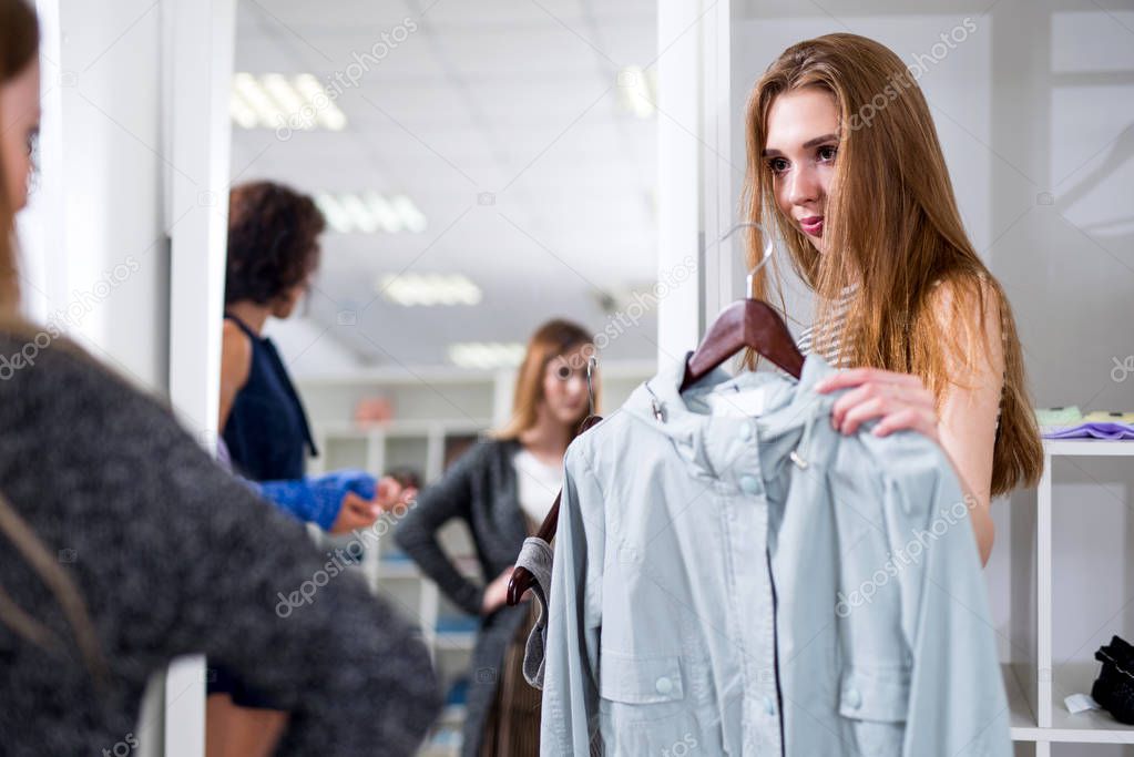 Female shop assistant offering two items of clothes to the customers in fashion store