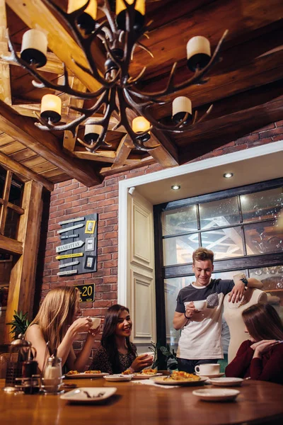 Students wearing casual clothes having a lunch break drinking coffee listening to their male friend talking in trendy coffee house — Stock Photo, Image
