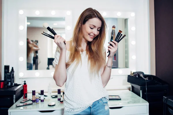 Young shy beautician posing with make-up brushes — Stock Photo, Image