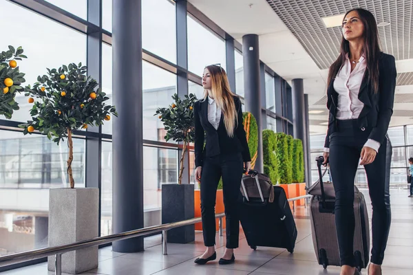 가방을 들고 공항 통로 통해 걷는 두 심각한 젊은 여성 동료 — 스톡 사진