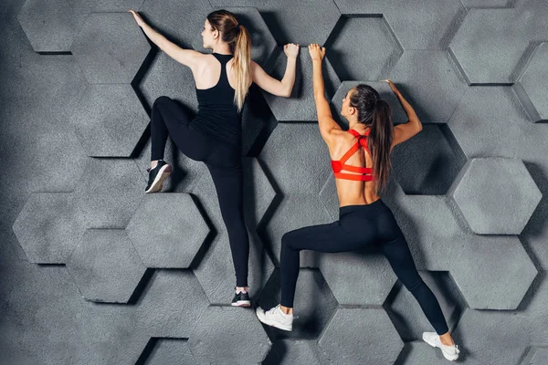 Fitte Frauen posieren wie ein Kletterer, der an einer dekorativen Wand hängt — Stockfoto