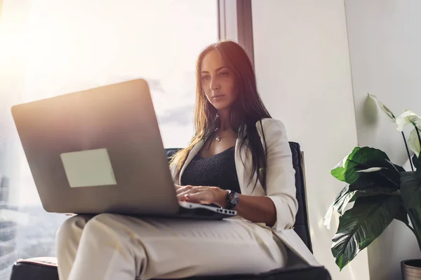 Eleganta affärskvinna med laptop sitter på fåtölj i loftlägenhet — Stockfoto