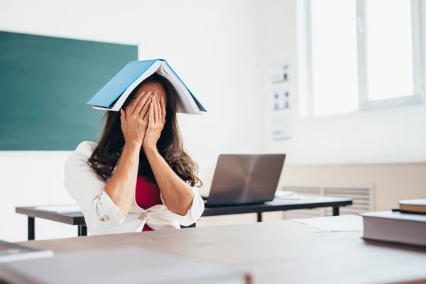 Unavená žena student sedí u stolu s knihou na hlavě — Stock fotografie