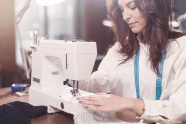 Dikiş makinesi ve genç kadın terzi bir atölyede otururken denemeye yakından görmek