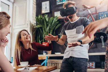 Genç adam sınama sanal gerçeklik kulaklık bir kafede oturup gülüyorsun neşeli çok kadın arkadaşları ise korkunç oyun oynarken çığlık