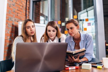 Birlikte laptop ve ders notları çalışma odası masasında oturan kullanarak üç Bayan üniversite öğrencileri