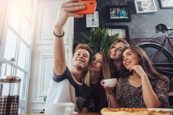 Group of cute teenagers taking selfie with cellphone while sitting in a restaurant with interior in retro style — Stock Photo, Image