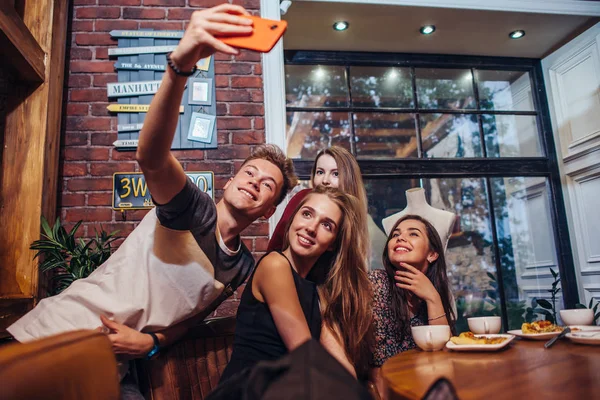 Amigos emocionados tomando selfie con teléfono inteligente sentado en la mesa teniendo una salida nocturna . — Foto de Stock