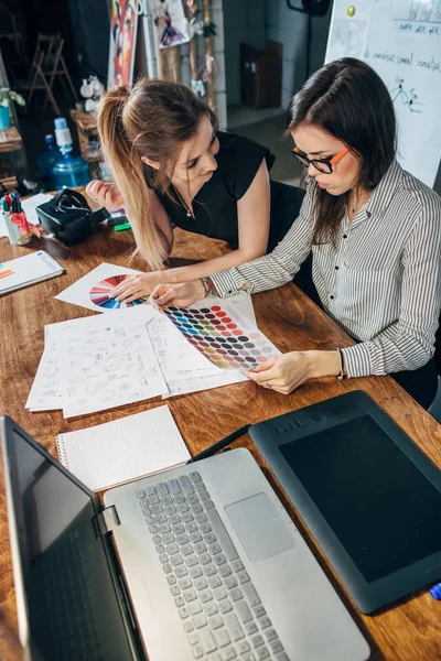 Mladá žena grafiků, sedí u stolu s notebookem, barevné grafy a některé náčrtky diskuse o nový projekt volba koncept — Stock fotografie
