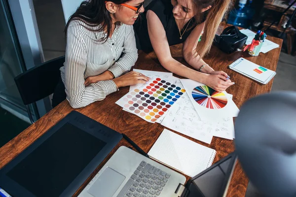 Dos arquitectas trabajando juntas usando muestras de color sentadas en el escritorio con computadora portátil, tableta gráfica en el estudio de diseño — Foto de Stock