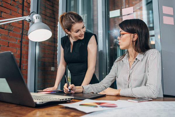 Команда дизайнеров женского интерьера рисует новый проект с помощью графического планшета, ноутбука и цветовой палитры, сидя за столом в современной студии
