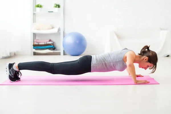 Vrouw doen push-ups op de vloer in haar woonkamer een oefening mat thuis passen — Stockfoto