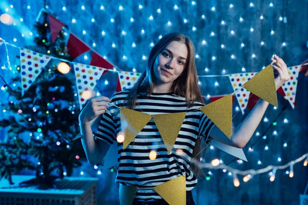 Una mujer joven decora la habitación Banderas, guirnaldas preparándose para la celebración de Navidad . —  Fotos de Stock