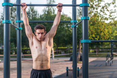 Parkta barfiks egzersizi yapan genç bir erkek atlet. Fitness adamı dışarıda çalışıyor.