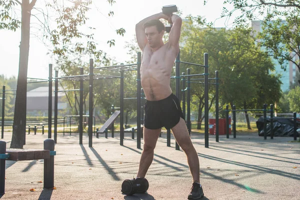 Muskularny mężczyzna atleta z ramionami podniesione robi ćwiczenia hantle. — Zdjęcie stockowe