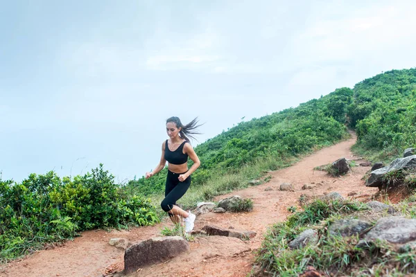 Mujer joven deportiva en pista de ropa deportiva negro que corre por el camino de la naturaleza de montaña. Chica en forma trotando cuesta abajo pista rocosa . —  Fotos de Stock