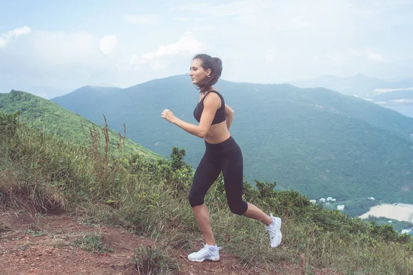 Ajuste jogger feminino exercitando, correndo subida com mar e montanhas no fundo — Fotografia de Stock