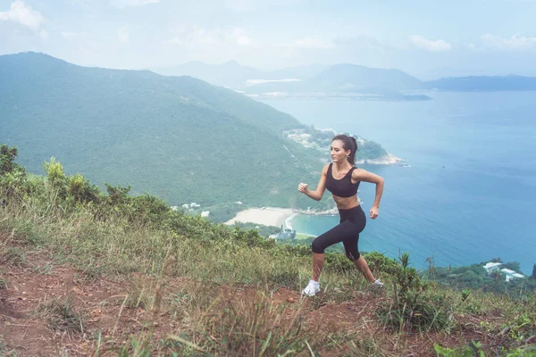 Sottile giovane atleta donna che fa esercizio cardio salendo la montagna con il mare sullo sfondo . — Foto Stock