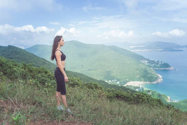 运动年轻女人站在山上 在阳光下的海洋和绿色的山风景 — 图库照片