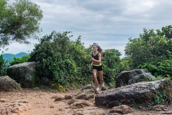 Vhodné sportovní mladá žena běží na špinavé kamenité cestě v horách v létě. — Stock fotografie