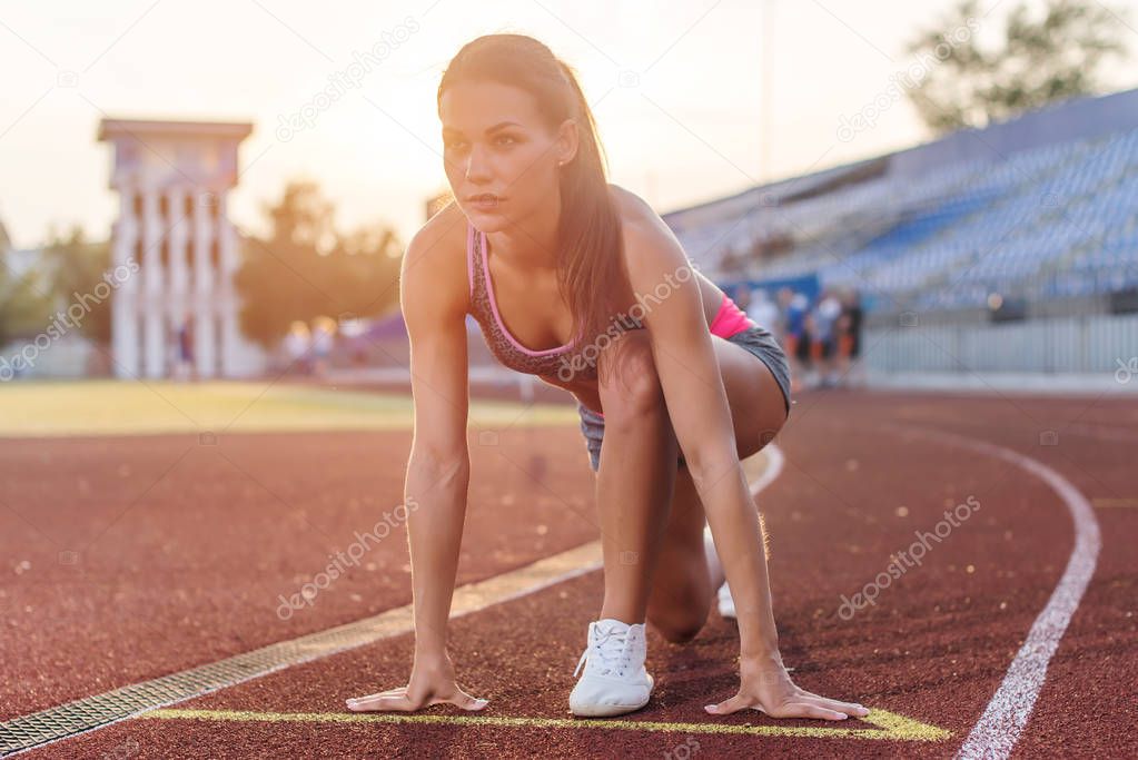 Women sprinters at starting position ready for race on racetrack.