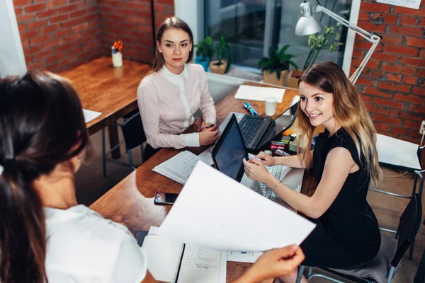 Team av business kvinnor som arbetar med papper använder bärbara datorer sitter vid skrivbord i office — Stockfoto