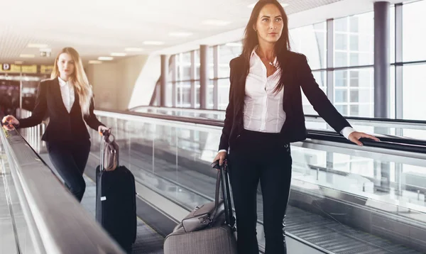 Due donne sicure di sé che indossano abiti formali in piedi sulla passerella in movimento in aeroporto — Foto Stock