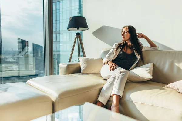 Портрет успешной деловой женщины в элегантном костюме, сидящей на кожаном диване после работы дома — стоковое фото