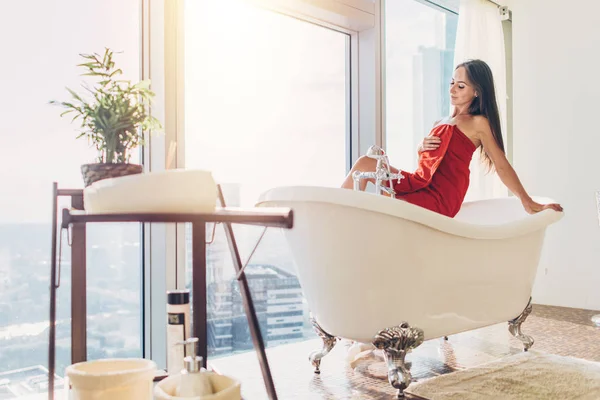 Slanke jonge vrouw in de handdoek zit op bad in de luxe badkamer — Stockfoto