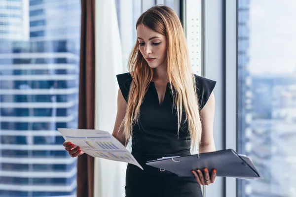 Kvinnliga finansiella analytiker håller papper studerar dokument stående mot fönster med stadsutsikt — Stockfoto