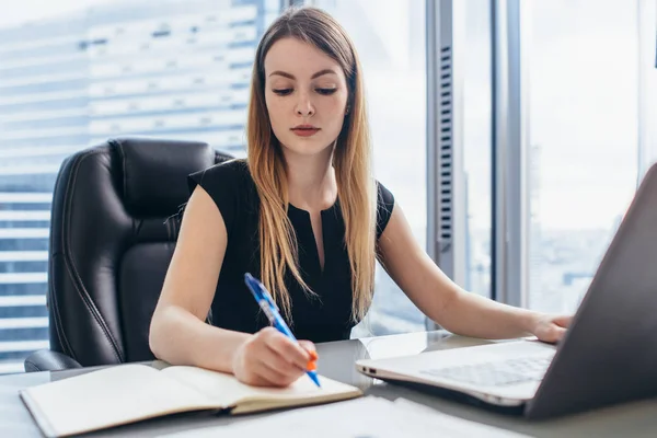 Koncentrované podnikatelka pracující psaní poznámek v poznámkovém bloku, sedí u stolu v kanceláři — Stock fotografie