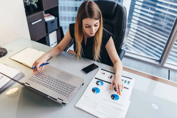 Mujer empresaria lee informe financiero analizando estadísticas apuntando a gráfico circular trabajando en su escritorio —  Fotos de Stock
