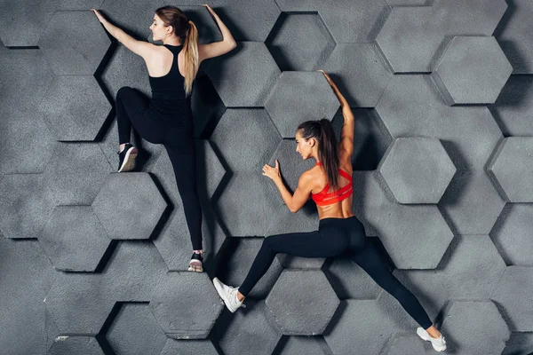 Fitte Frauen posieren wie ein Kletterer, der an einer dekorativen Wand hängt — Stockfoto