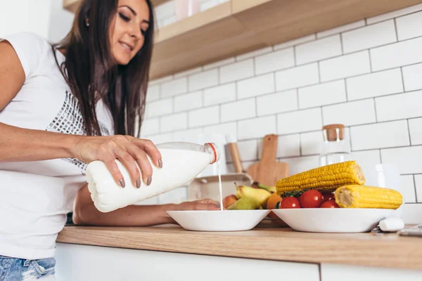 Mujer desayunando vertiendo leche en un tazón con muesli en la cocina — Foto de Stock