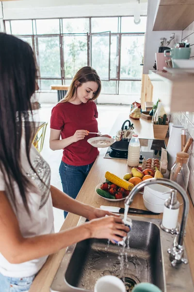 Two girls friends in kitchen preparing breakfast cooking and washing dishes — Stock Photo, Image