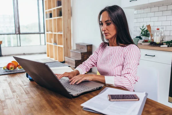 Kobieta za pomocą laptopa siedząc w kuchni i pracy na laptopie. — Zdjęcie stockowe